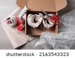 Small photo of Open box with wrapped items, adhesive tape, scissors, paper and bubble wrap on wooden table, flat lay