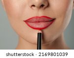 Young woman applying beautiful red lip pencil on grey background, closeup