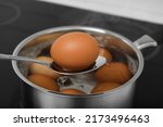 Spoon with boiled egg above saucepan on electric stove, closeup