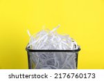 Trash bin with shredded paper strips on yellow background