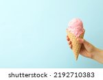 Woman holding waffle cone with delicious pink ice cream on light blue background, closeup. Space for text