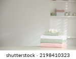 Stack of clean soft towels with orchid flowers on white table indoors. Space for text
