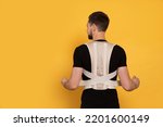 Small photo of Man with orthopedic corset on orange background, back view. Space for text