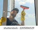 Small photo of Man cleaning glass with squeegee indoors, view from inside