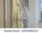 Worker in uniform and respiratory mask insulating wall indoors