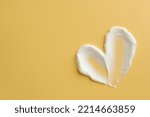 Samples of face cream in shape of heart on yellow background, top view. Space for text