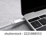 USB cable with type C connector plugged into laptop port on grey table, closeup