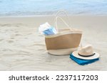 Bag with blanket, beach towel and straw hat on sandy seashore, space for text