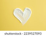 Samples of face cream in shape of heart on yellow background, top view