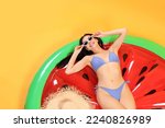 Happy young woman with beautiful suntan, sunglasses and hat on inflatable mattress against orange background, above view
