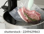 Small photo of Woman putting vacuum packed meat into pot with sous vide cooker in kitchen, closeup. Thermal immersion circulator
