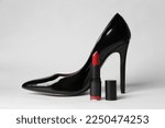 Beautiful red lipstick and black high heeled shoe on white background