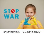 Stop war. Little girl making heart with her hands painted in colors of Ukrainian flag on light background