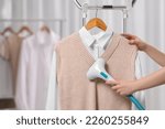 Small photo of Woman steaming clothes on hanger at home, closeup