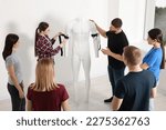 Small photo of Group of people learning how to apply medical tourniquet on mannequin indoors
