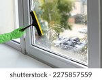 Small photo of Woman cleaning glass with squeegee indoors, closeup