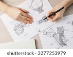 Jeweler drawing sketch of elegant ring on paper at wooden table, top view
