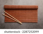 Rolled bamboo mat and chopsticks on grey table, top view. Space for text