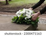 Small photo of Woman with wreath of flowers near tombstone outdoors, closeup. Funeral attribute