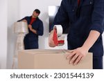 Small photo of Male mover packing box with adhesive tape in house, closeup. Space for text