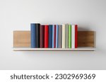 Many hardcover books on wooden shelf near white wall