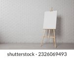 Small photo of Wooden easel with blank canvas near white brick wall indoors. Space for text