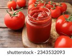 Jar of tasty ketchup and tomatoes on wooden table, closeup