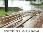 Wooden bench with water drops outdoors, closeup. Rainy weather