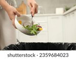 Small photo of Woman throwing vegetable salad into bin indoors, closeup