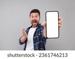Small photo of Surprised man showing smartphone in hand on light grey background