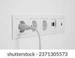Small photo of Many power sockets with plug, ethernet and TV coax plates on white wall indoors