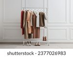 Rack with different stylish women`s clothes and shoes near white wall indoors