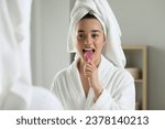 Happy woman brushing her tongue with cleaner near mirror in bathroom