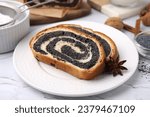 Slices of poppy seed roll and anise star on white textured table, closeup. Tasty cake