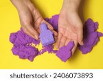 Small photo of Woman playing with kinetic sand on yellow background, top view