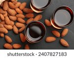 Glasses with tasty amaretto liqueur and almonds on dark gray table, flat lay