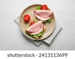 Small photo of Plate of tasty sandwiches with boiled sausage, tomato and lettuce on white wooden table, top view