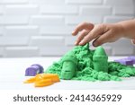 Small photo of Little child playing with green kinetic sand at white table, closeup. Space for text