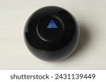 Small photo of Magic eight ball with prediction Answer Unclear Ask Later on white table, above view