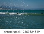 Small photo of DANA POINT, CA, U.S.A. - AUG. 26, 2023: Artistic photo of the distant back of a surfer on small waves with ocean spray coming up at Doheny State Beach, in Dana Point, California.
