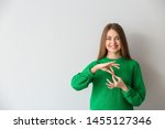 Small photo of Young deaf mute woman using sign language on light background