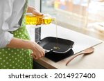 Woman pouring sunflower oil onto frying pan in kitchen