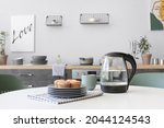 Electric kettle, cup of tea and pastry on kitchen table