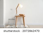 Glowing lamp and books on table near light wall