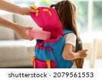 Mother putting school lunch in backpack of her little daughter at home