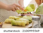 Small photo of Woman preparing tasty stuffed cabbage rolls on table in kitchen, closeup