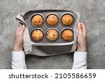 Woman holding baking tin with tasty cranberry muffins on grunge background