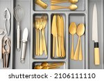 Open kitchen drawer with golden cutlery and utensils, closeup