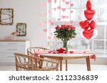 Glasses of champagne, engagement ring and flowers on dining table in room decorated for Valentine's day