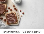Small photo of Board of bread with chocolate paste and hazelnuts on white background, closeup